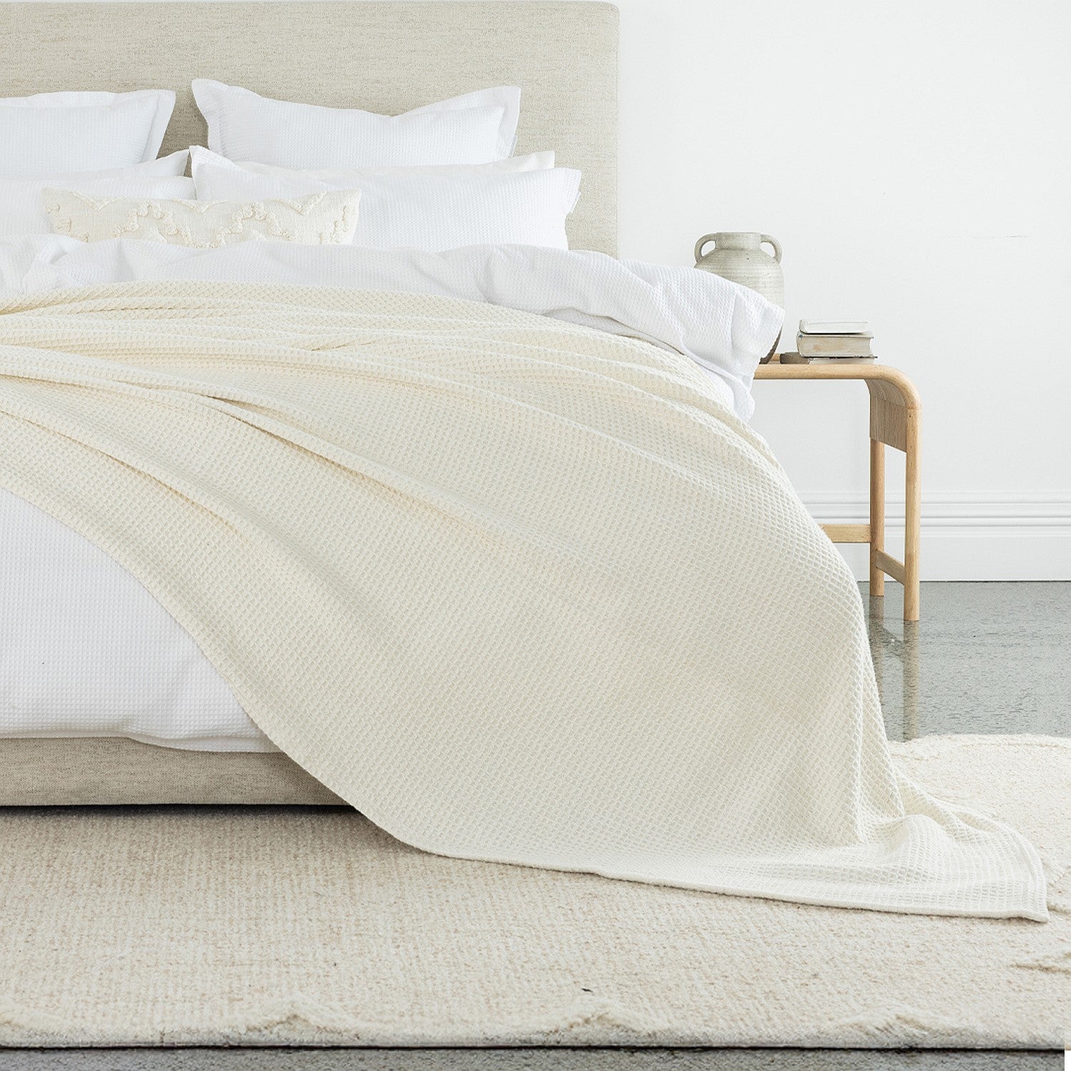 A richly textured ivory waffle-weave blanket draped across crisp white bedding adds depth, warmth, and timeless elegance to the bedroom.