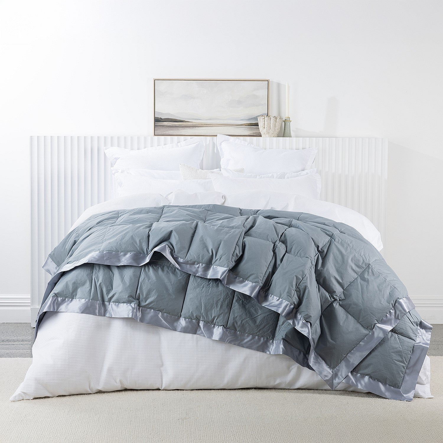 A luxuriously soft feather and down blanket in a dusty blue tone, finished with satin trim for an elegant and inviting bedroom look.