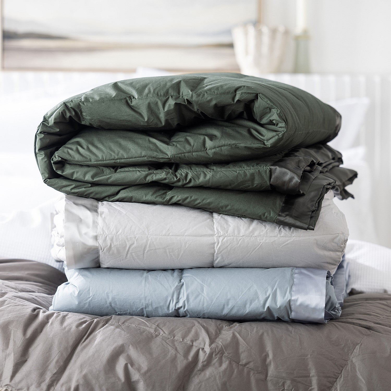 A refined collection of feather and down blankets layered elegantly to showcase their plush comfort and satin-trim detailing.