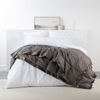 A luxuriously soft feather and down blanket in a stone brown tone, finished with elegant satin trim for a refined and inviting bedroom aesthetic.