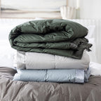 A refined collection of feather and down blankets layered elegantly to showcase their plush comfort and satin-trim detailing.