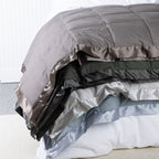 A refined collection of feather and down blankets layered elegantly to showcase their plush comfort and satin-trim detailing.