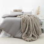 An ultra-plush faux-fur blanket in soft taupe tones, designed to drape beautifully across the bed with rich texture and cozy warmth.