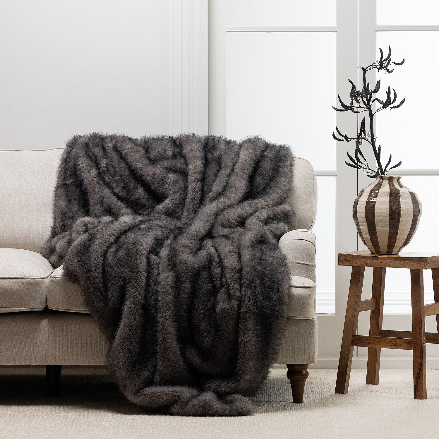 A richly textured charcoal faux-fur throw is elegantly draped over a soft neutral sofa, creating a warm and sophisticated living space.