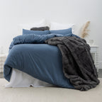 A plush charcoal faux-fur throw draped over deep blue bedding adds rich texture and warmth to this calm, contemporary bedroom setting.