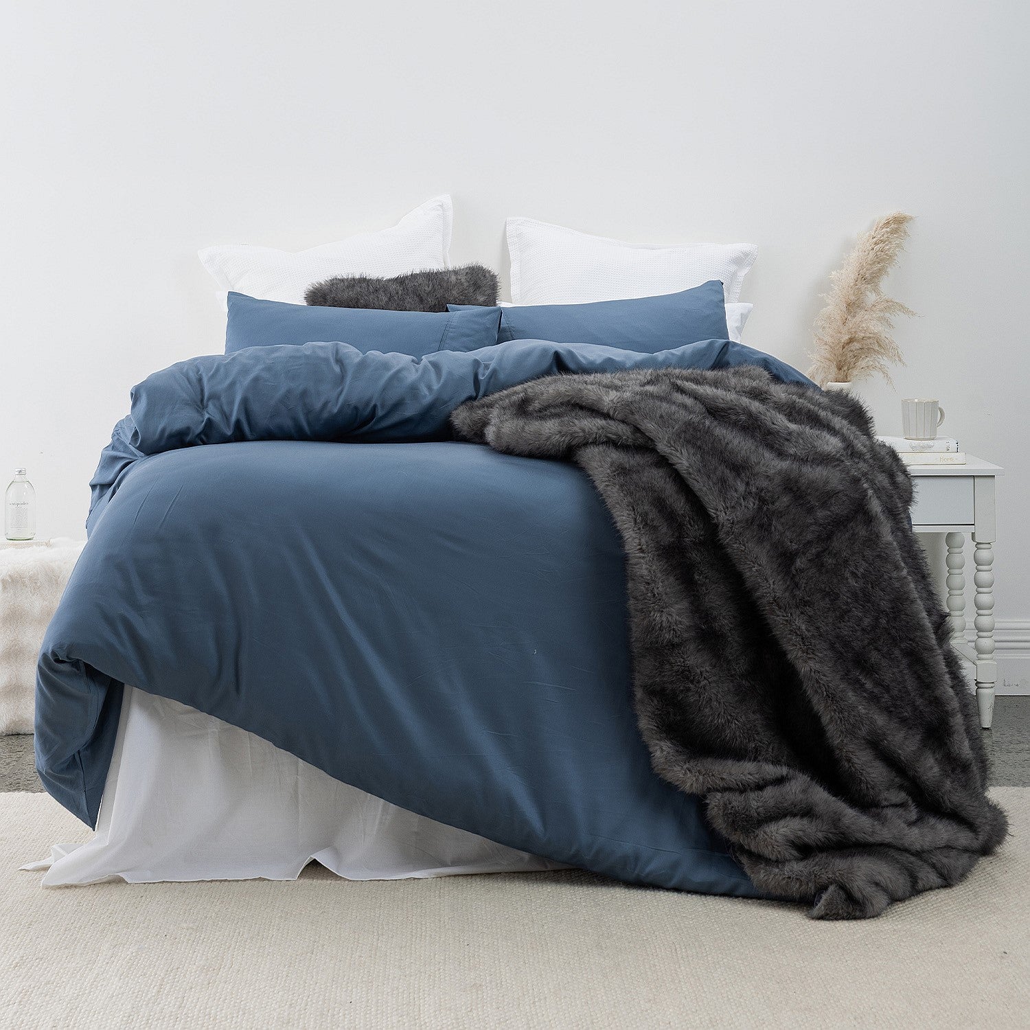 A plush charcoal faux-fur throw draped over deep blue bedding adds rich texture and warmth to this calm, contemporary bedroom setting.