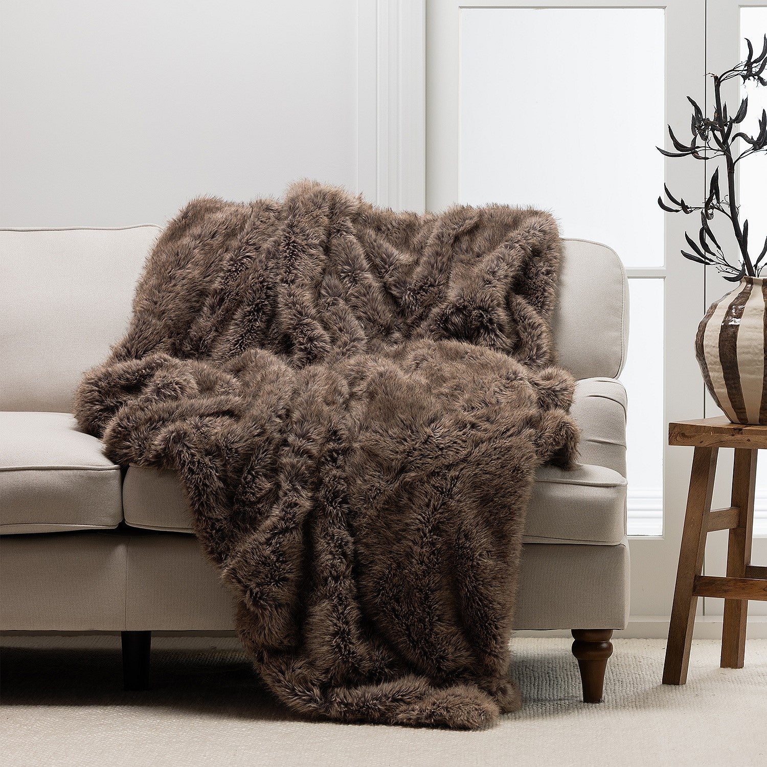 A richly textured taupe faux-fur throw draped over a neutral sofa brings warmth, softness, and understated luxury to the living space.