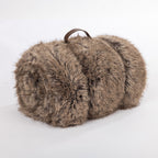 A luxuriously soft taupe faux-fur throw, neatly rolled and finished with a rich brown leather carry handle for an elegant, cozy touch.