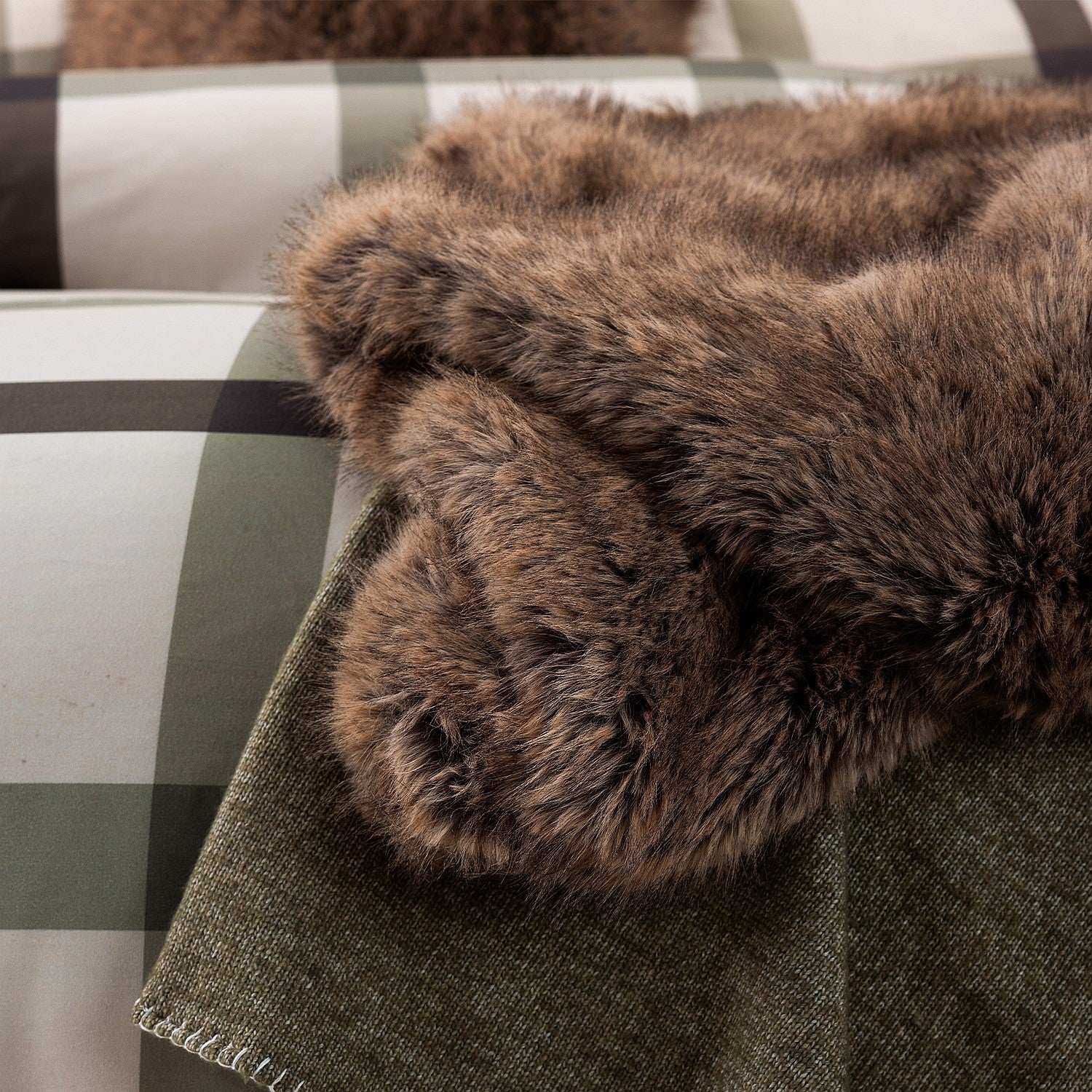 A plush taupe faux-fur throw is styled atop classic check-patterned bedding, creating a warm and inviting layered look.