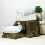 A refined collection of ultra-soft faux-fur throws, blankets and matching cushions in muted ivory, olive, and silver tones, styled for a warm and contemporary living space.