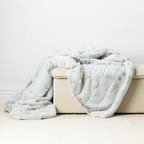 A beautifully plush faux-fur throw in a soft icy grey tone, draped effortlessly to highlight its velvety texture and inviting warmth.
