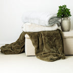 A sophisticated arrangement of plush faux-fur blankets in silver, ivory, and olive tones, layered effortlessly to create a warm and inviting interior setting.