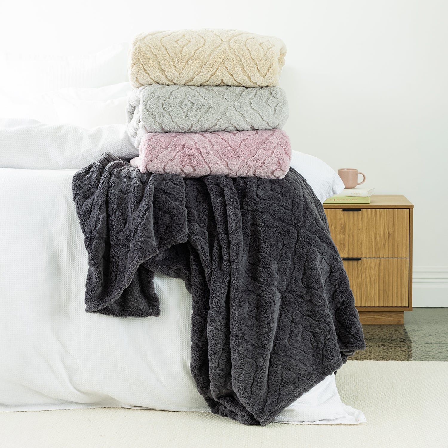 Stack of 4 Embossed fleece blankets styled on the end of bed