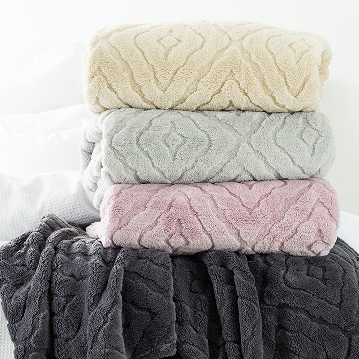 Stack of 4 Embossed fleece blankets styled on the end of bed