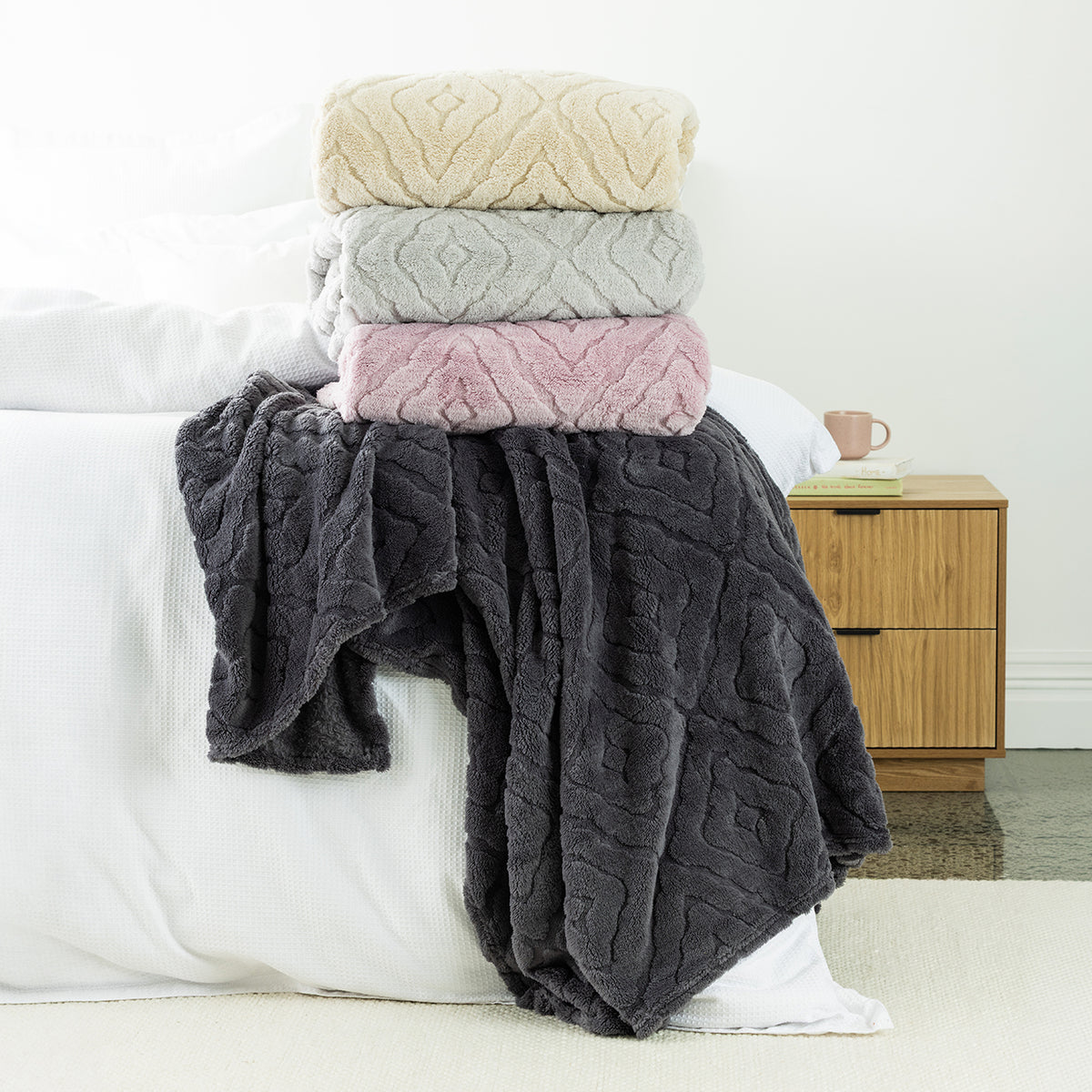 Stack of 4 Embossed fleece blankets styled on the end of bed