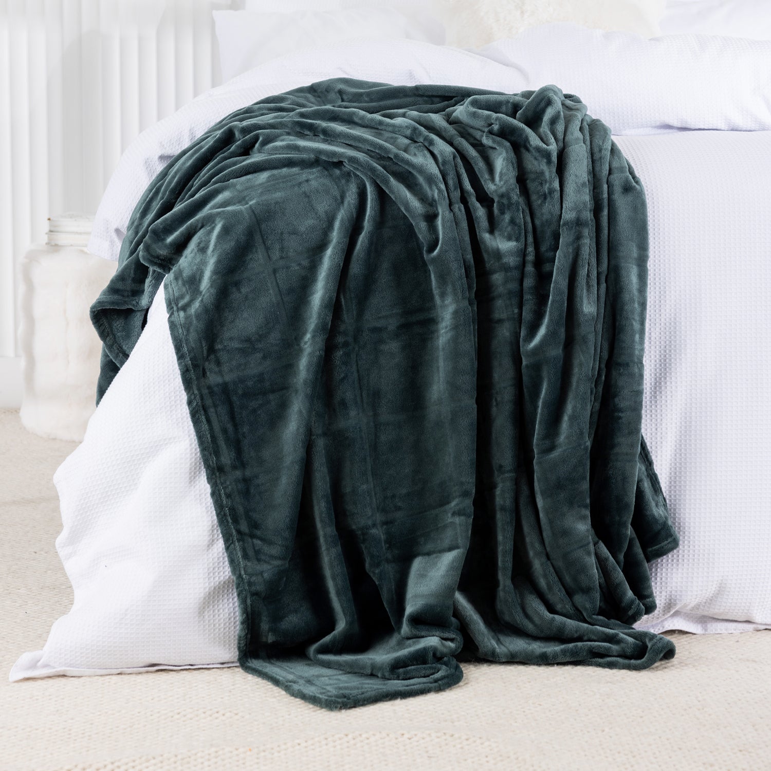 Green blanket draped over a white bed