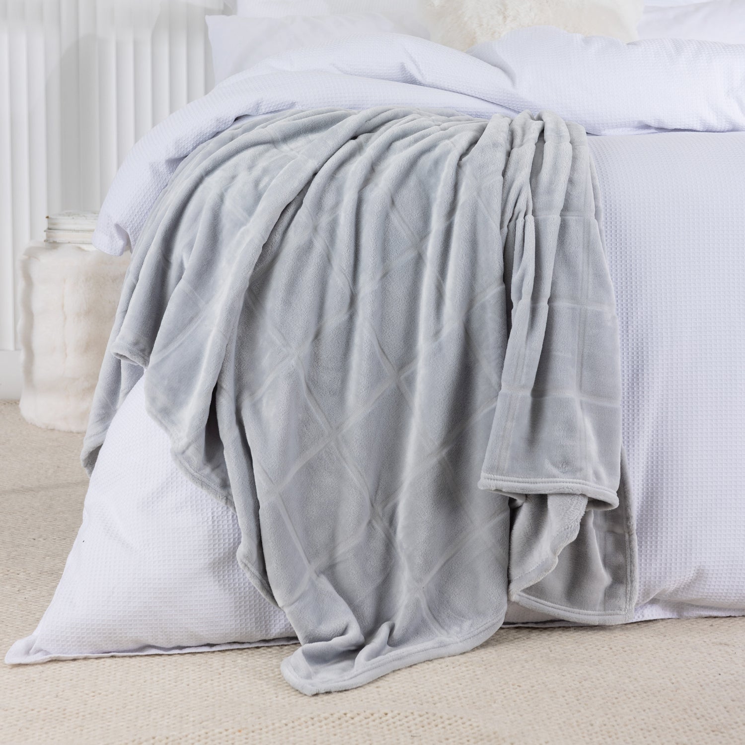 Gray blanket draped over a white bed in a bedroom setting