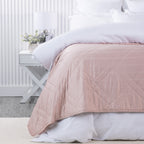 Bambou Summer Blanket in Blush styled on a white bed, featuring a soft pink tone and large diamond quilted pattern.