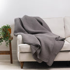 Charcoal waffle weave blanket draped over the arm of a cream sofa, showcasing its textured finish in a contemporary living room.
