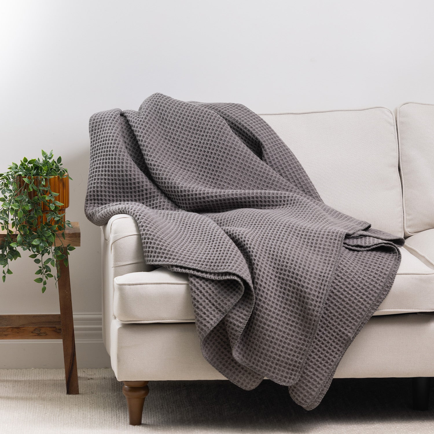 Charcoal waffle weave blanket draped over the arm of a cream sofa, showcasing its textured finish in a contemporary living room.