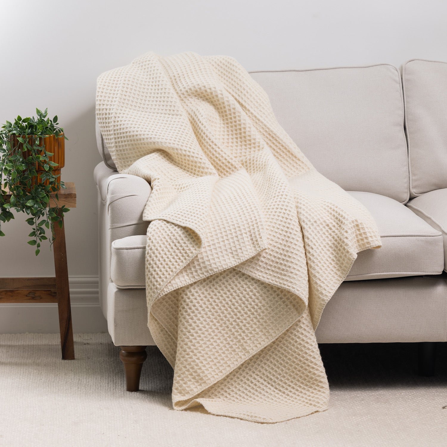 Ivory waffle weave blanket draped over the arm of a cream sofa, featuring a cosy textured finish in a bright contemporary living room.