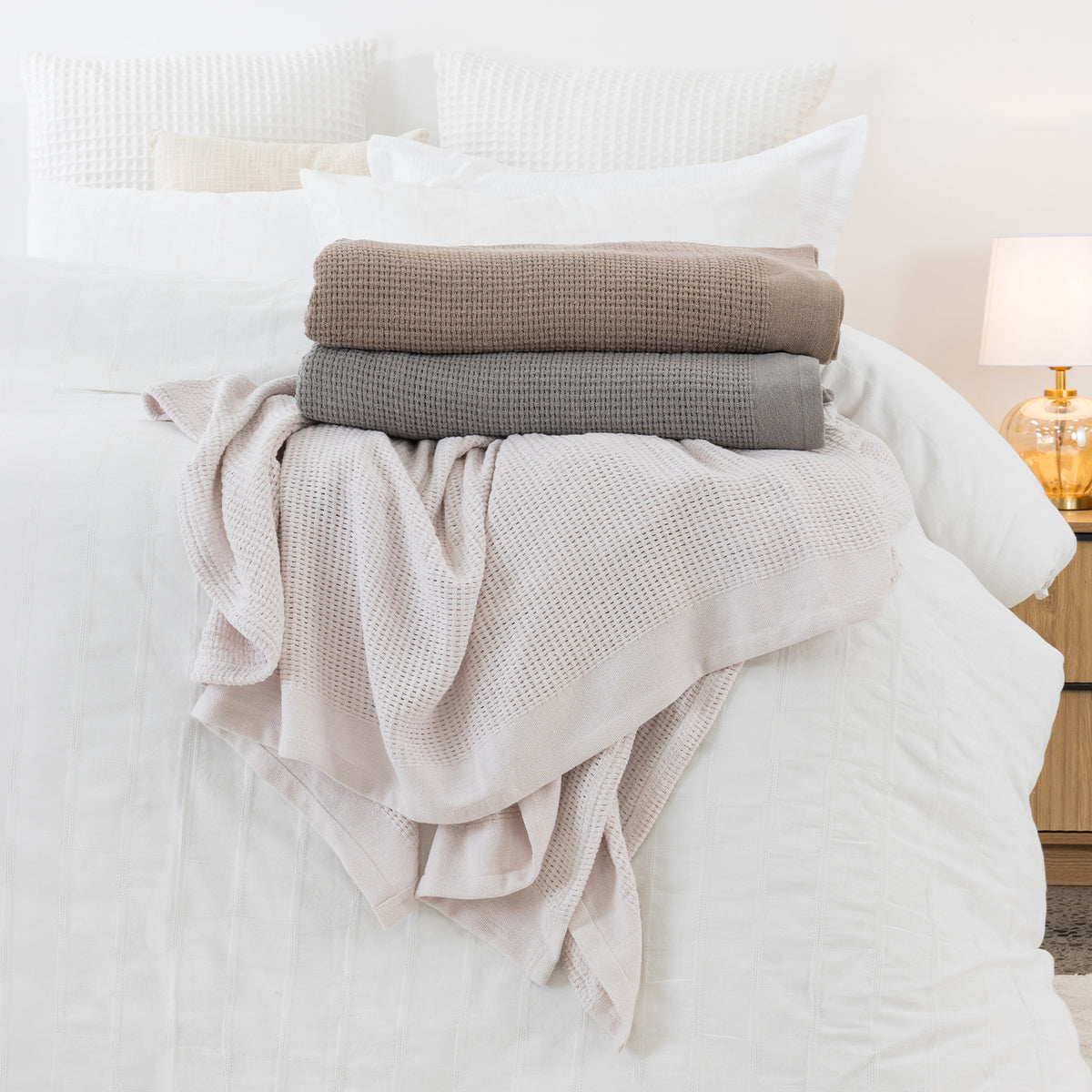 Mocha, Dove and Linen aircell blankets styled together on a white bed, showcasing their textured waffle weave and soft tonal colours.