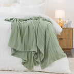 Sage aircell blanket draped across a white bed, showcasing its lightweight textured knit and subtle striped pattern.