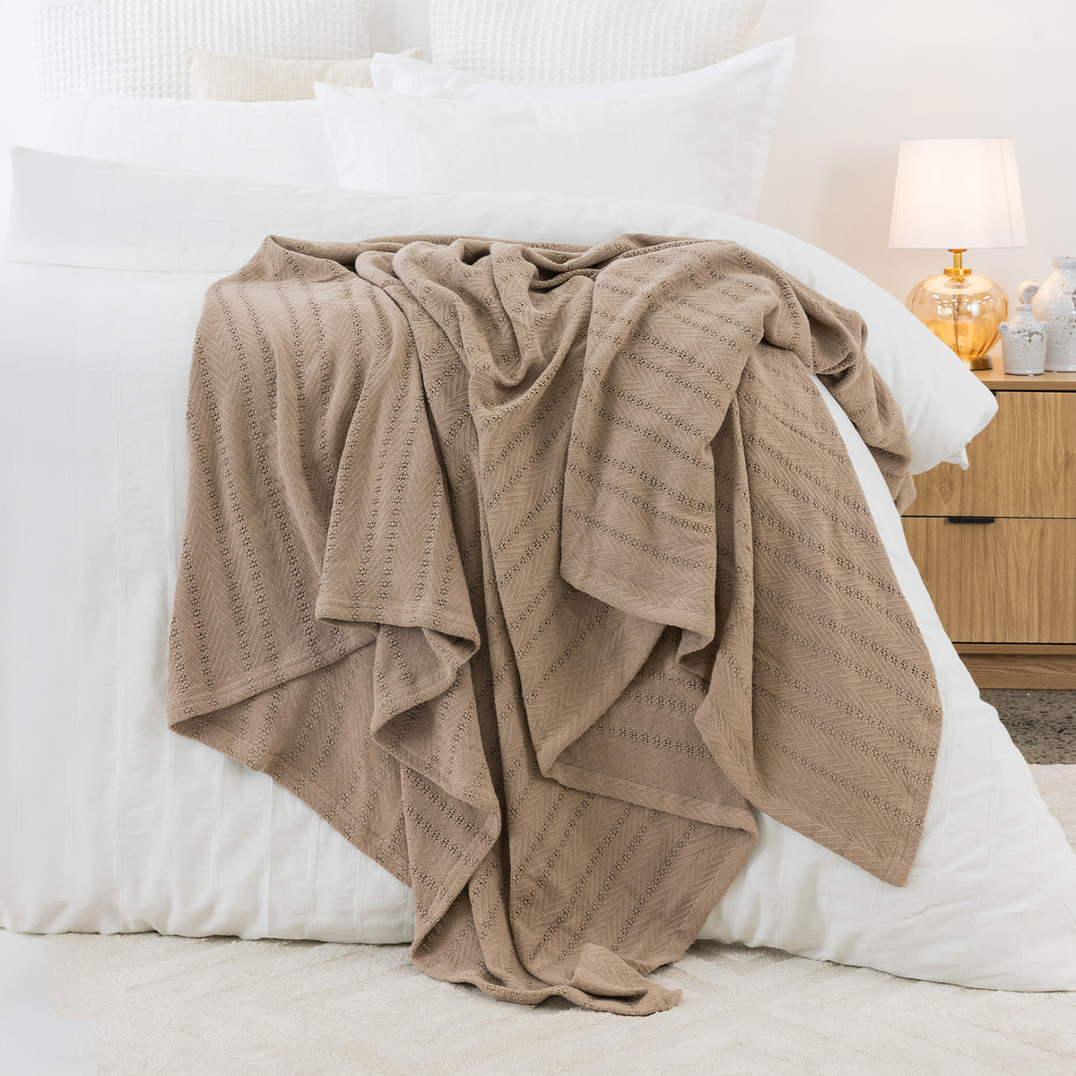 Taupe aircell blanket draped across a white bed, showcasing its lightweight textured knit and subtle striped pattern.