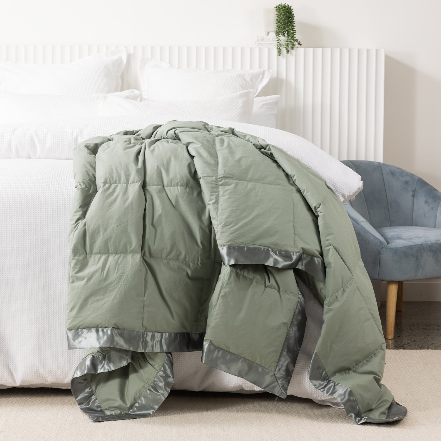 Fieldcrest duck down blanket in Moss, draped over the end of a white bed to showcase the soft quilted design with satin trim.