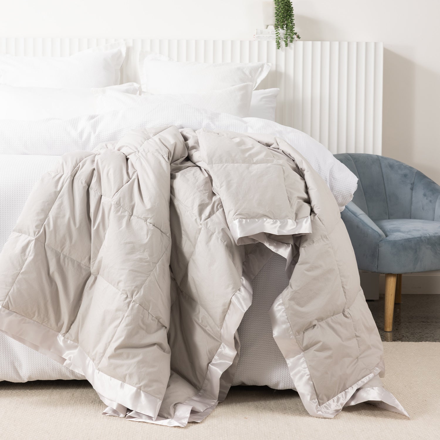 Fieldcrest duck down blanket in Pumice, draped over the end of a white bed to showcase the soft quilted design with satin trim.