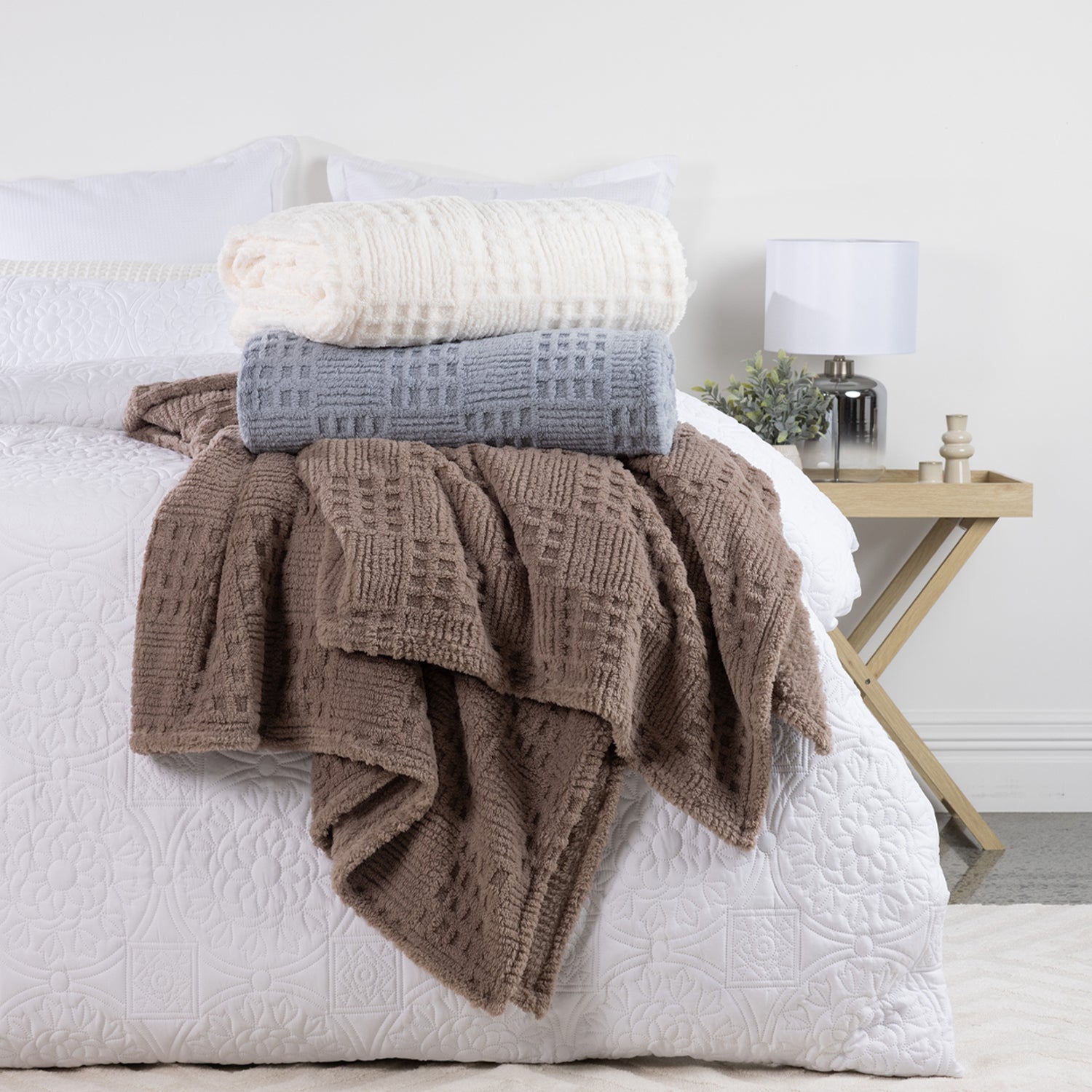Solace Trellis Blankets styled on a white bed, featuring White, Silver Blue and Driftwood colourways with coordinating textured designs.