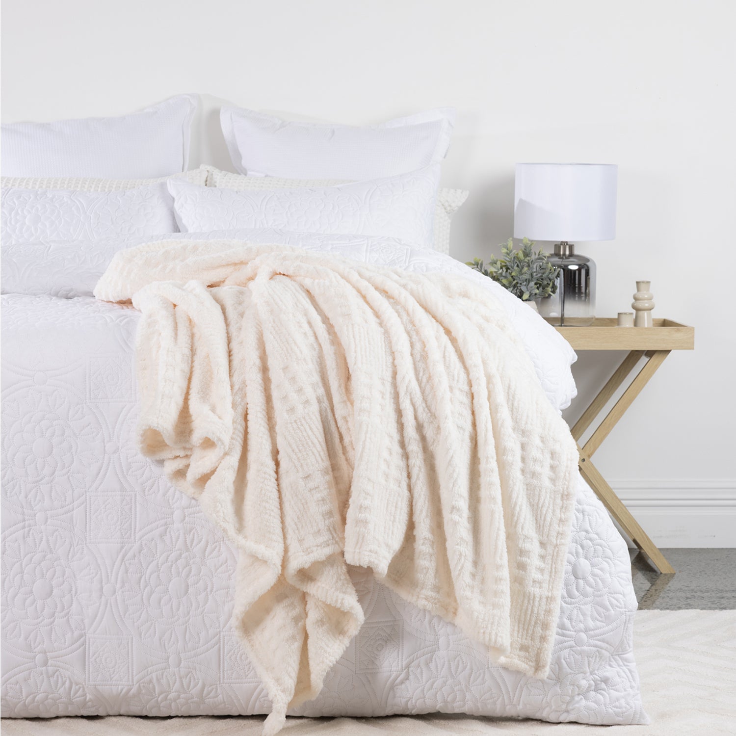 Silver Blue Solace Trellis Blanket draped across a white bed, showing its soft plush texture and raised trellis pattern.