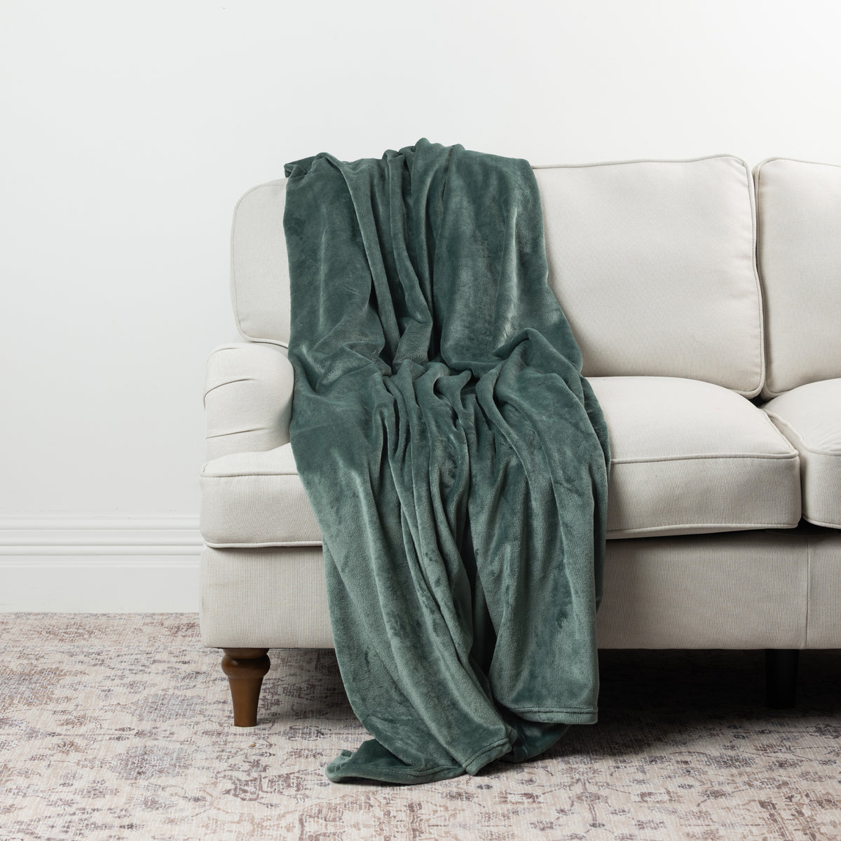 Pine green Home Co. Super Plush Blanket styled over a neutral sofa, showing its rich colour and soft plush finish.
