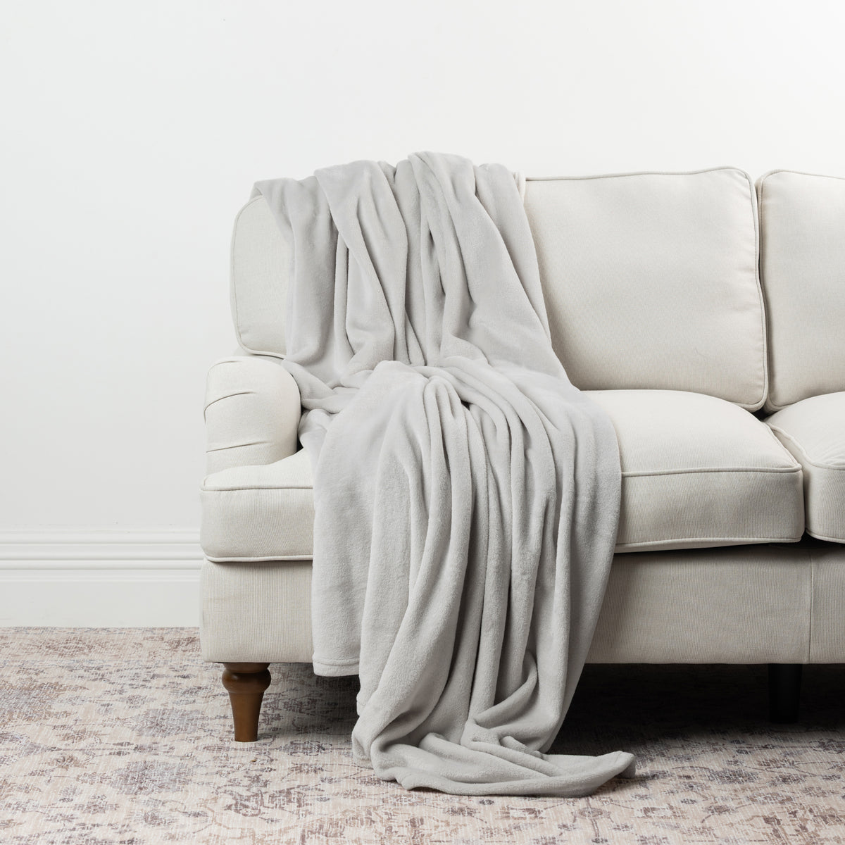 Silver Home Co. Super Plush Blanket draped over a neutral sofa, highlighting its soft texture and light grey tone.