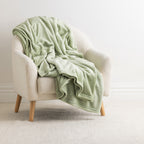 Home Co. Malange Blanket in Green Tea draped over a cream boucle armchair in a bright neutral living space.