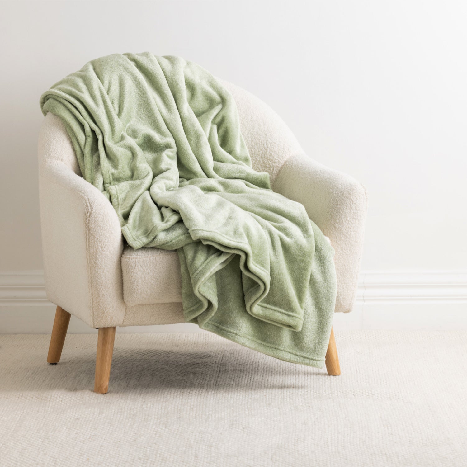 Home Co. Malange Blanket in Green Tea draped over a cream boucle armchair in a bright neutral living space.