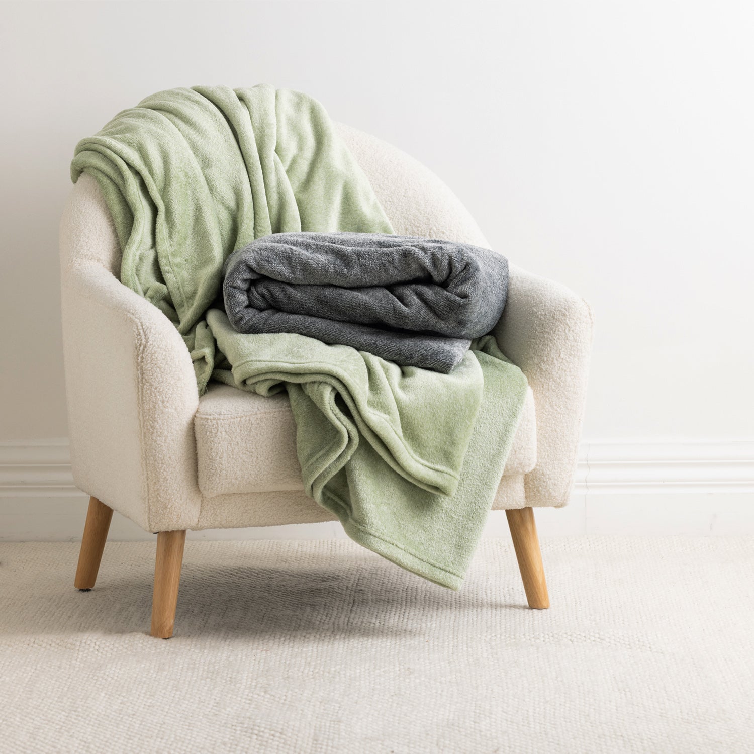 Home Co. Malange Blankets in Green Tea and Grey styled together on a cream boucle armchair in a neutral interior.