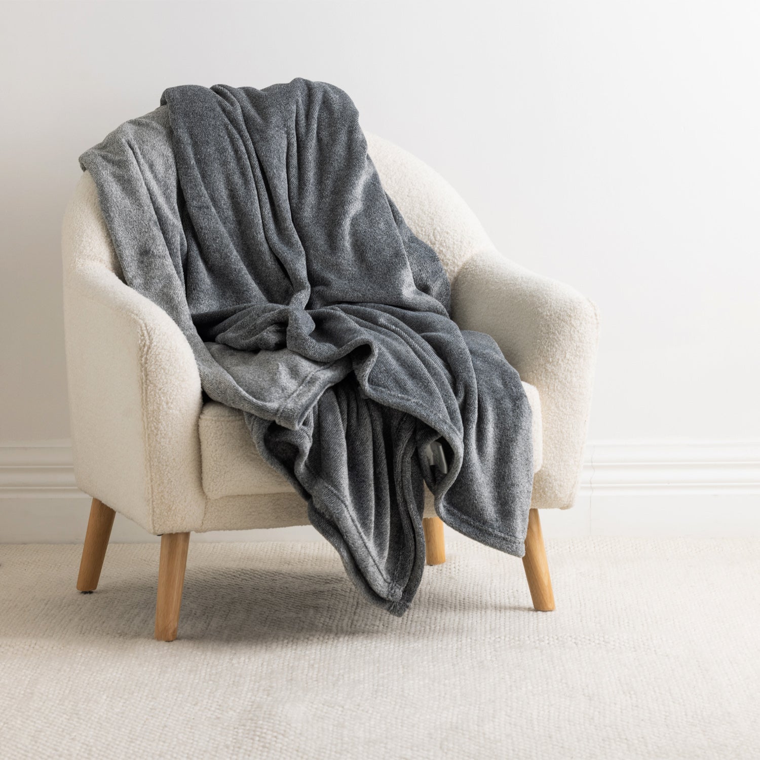 Home Co. Malange Blanket in Grey draped over a cream boucle armchair, showing its soft plush texture and relaxed folds.