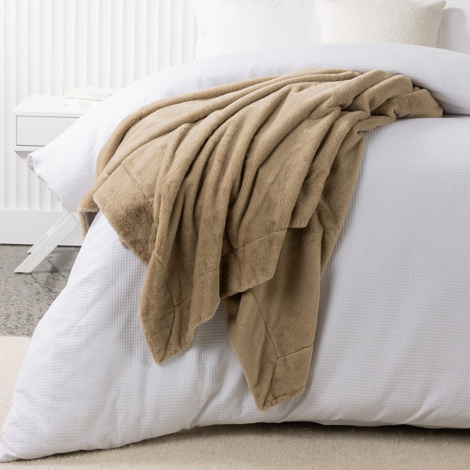 A luxuriously soft latte faux fur blanket is casually draped across crisp white bedding, adding warmth, texture and inviting comfort to the bedroom.