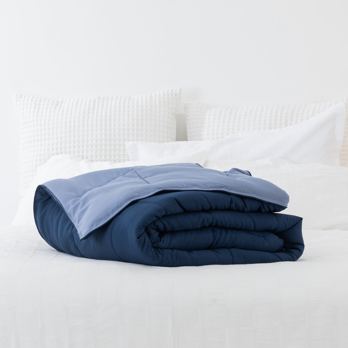 Blue: Folded navy and soft blue two-tone quilted blanket displayed on a neatly styled bed.