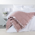 Fieldcrest Duck Down Blanket in Blush draped across a white bed, featuring quilted panels and a coordinating satin border.