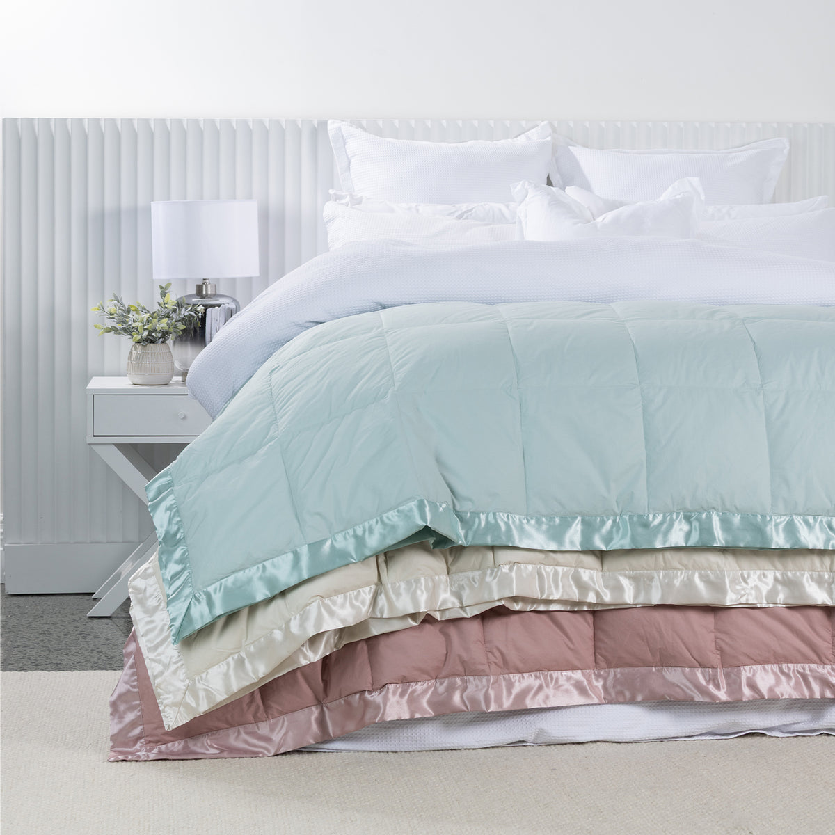 Fieldcrest Duck Down Blankets in Duckegg, Natural and Blush layered across a white bed, featuring quilted panels and satin borders.