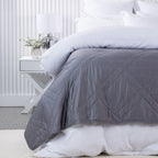 Bambou Summer Blanket in Charcoal styled on a white bed, showing the deep grey colour and diamond quilting.