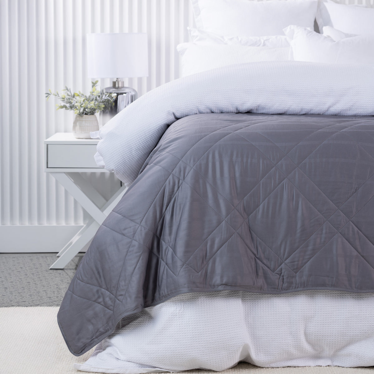 Bambou Summer Blanket in Charcoal styled on a white bed, showing the deep grey colour and diamond quilting.