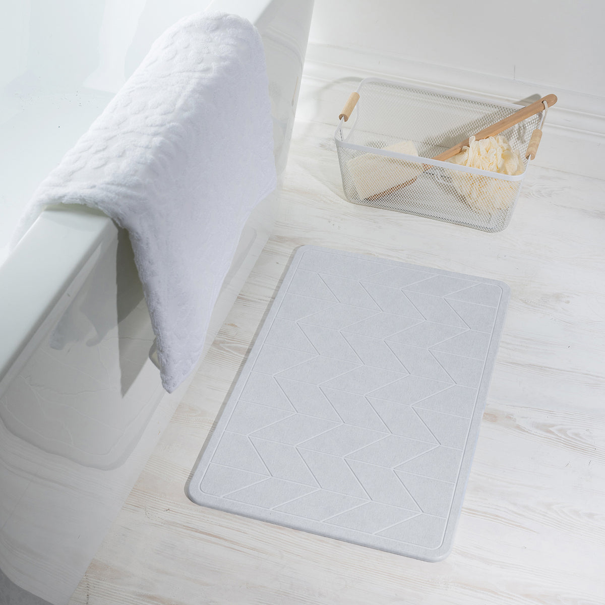 Algodon Dri Stone Bath Mat Light Grey displayed beside a white bathtub in a bright bathroom.