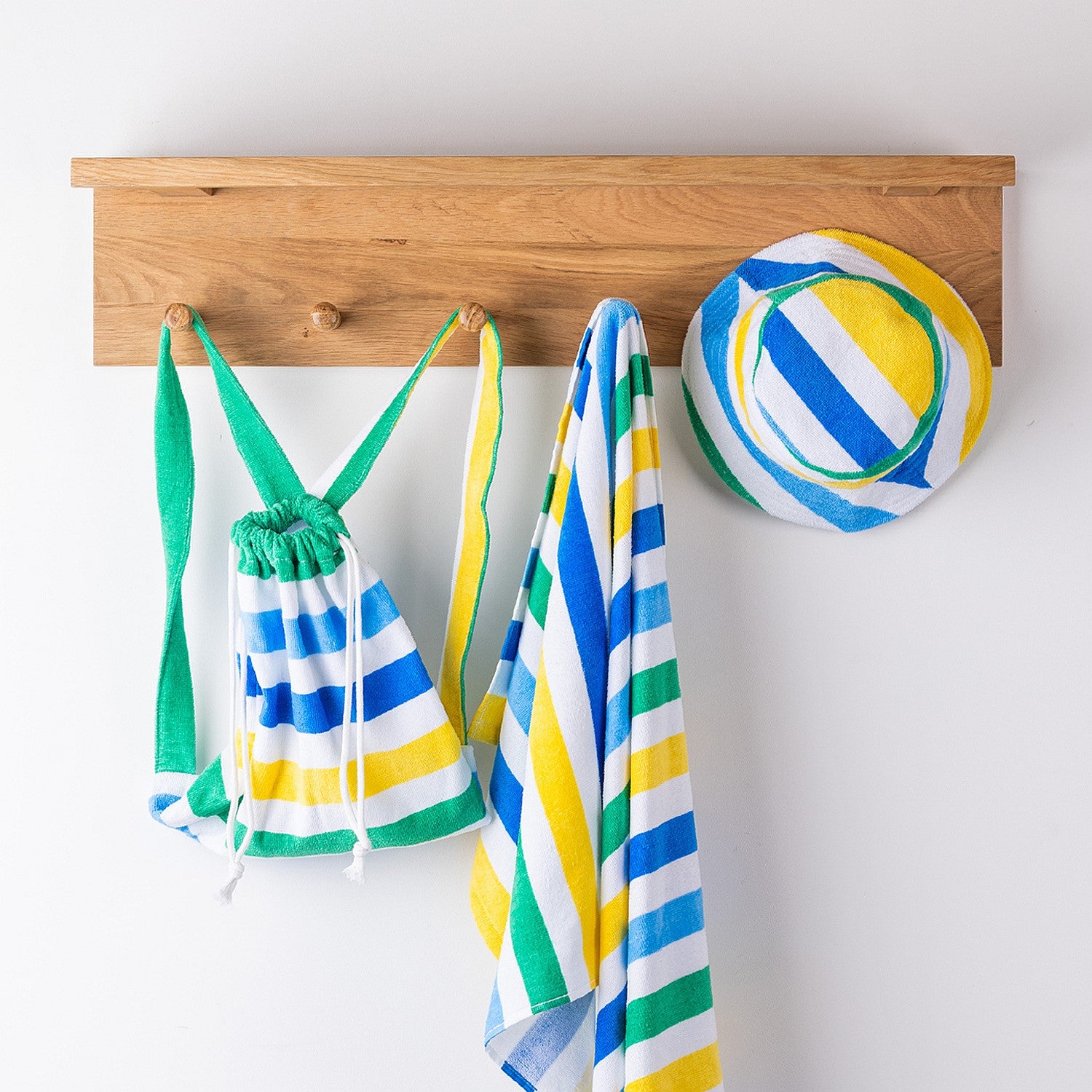 Striped kids hooded towel and matching bag and hat hanging on wooden hooks.