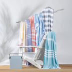Collection of striped beach towels in assorted pastel and neutral colours draped over a white outdoor lounge chair in a relaxed summer setting.