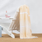 Yellow and white striped beach towel draped over a white outdoor lounge chair in a relaxed summer setting.