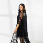 A woman modeling a black slip dress with a sheer black lace kaftan cover-up draped over her, set against a bright white studio background.