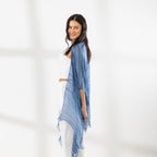 A woman modeling a Chambray striped fringed Kaftan or wrap over a white crop top and white Pants, standing against a white studio wall.